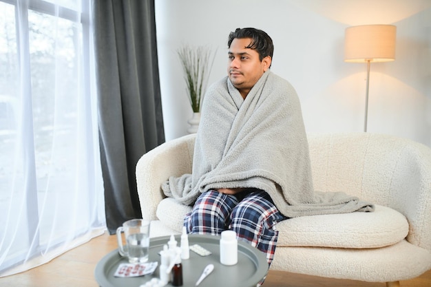 Foto conceptos de salud y gente enfermo joven indio con manta con dolor de cabeza o fiebre en casa
