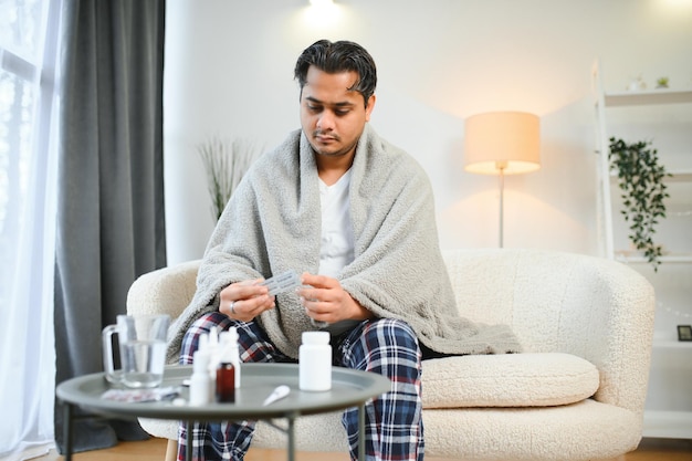 Foto conceptos de salud y gente enfermo joven indio con manta con dolor de cabeza o fiebre en casa