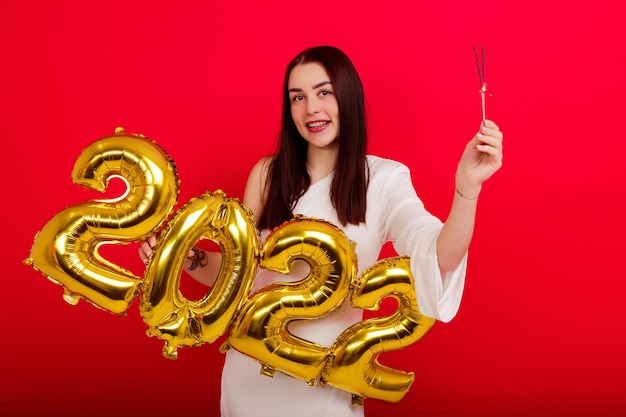 Concerto de Natal - uma jovem sorridente em um vestido branco segurando os números 2022 e brilhos