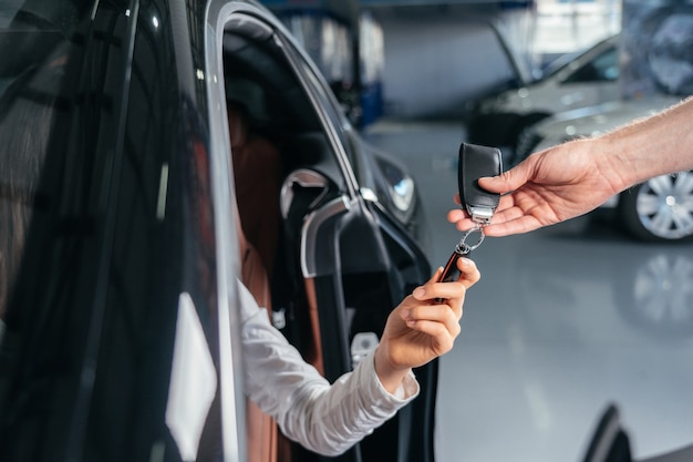 Concesionario de automóviles está dando la llave para un automóvil nuevo a una joven