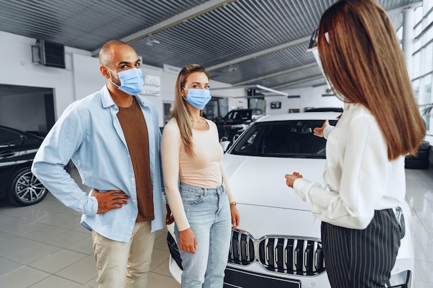 Concesionario de automóviles de mujer consultando a los compradores con protector facial médico