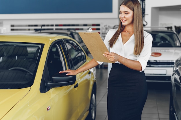 Concesionario de automóviles mujer joven atractiva de pie en la sala de exposición cerca de un coche nuevo