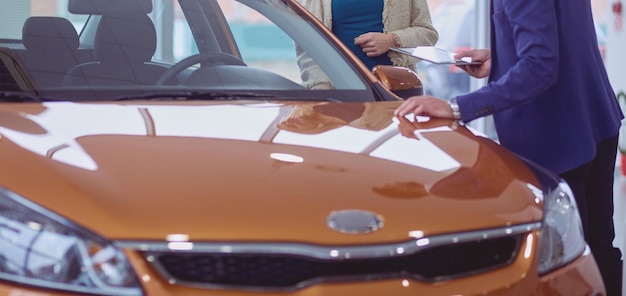 Concesionario con mujer se encuentra cerca de un coche nuevo en la sala de exposición