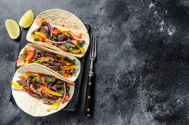 Conchas de tacos mexicanos com carne bovina, cebola, tomate e pimentão. Fundo preto. Vista do topo. Copie o espaço.