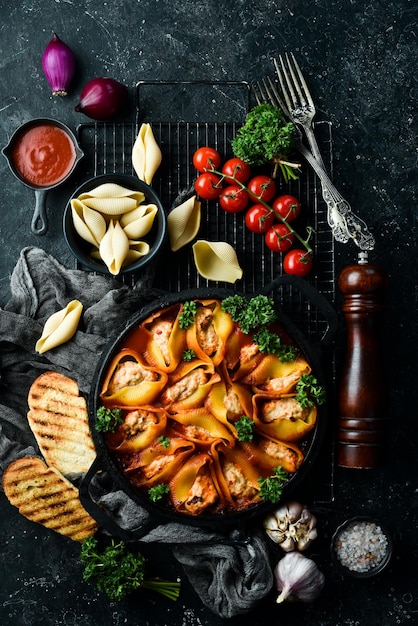 Conchas de pasta al horno con tomates de carne y parmesano en una sartén sobre un fondo de piedra negra