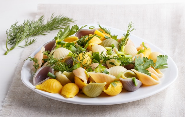 Conchiglie coloriu a massa com greengrocery fresco em uma toalha de mesa de linho na mesa de madeira branca.