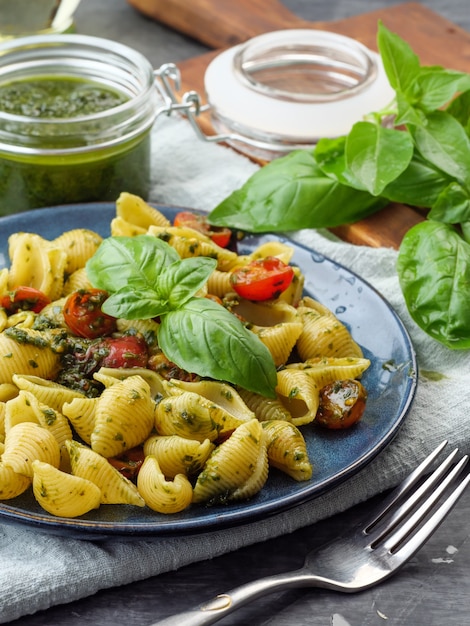 Conchiglie rigate a tradicional massa italiana com molho pesto e tomates refogados na mesa.