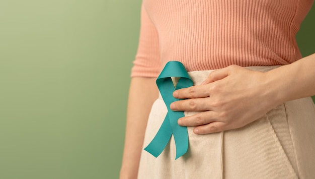 Foto concientización sobre el cáncer de ovario y cuello uterino mujer sosteniendo una cinta verde azulado en la parte inferior del abdomen útero sistema reproductor femenino salud de la mujer sop y ginecología