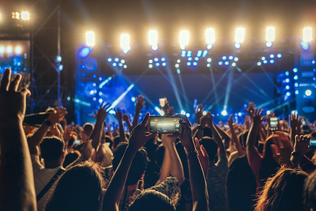 Concierto de la mano de un club de fans de música usando un teléfono celular para grabar video o transmisión en vivo