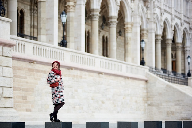 Concurso feminino sorrindo em pé contra a grande arquitetura da cidade de Budapeste. Palácio do Parlamento em Budapeste, Hungria. Outono