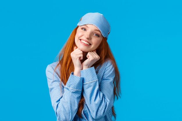 Concurso, mulher ruiva feminina com sorriso bonito, inclinar a cabeça segurando os braços perto do rosto pose linda, sorrindo como em pé em roupa de dormir e dormir máscara, pronto ter bons sonhos, parede azul