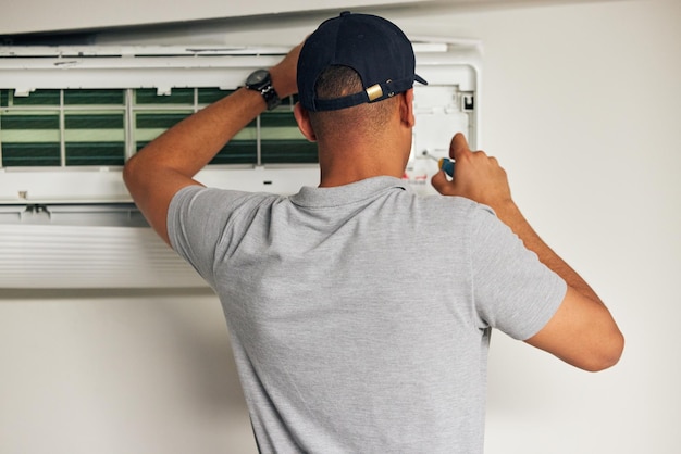 Condicionador de ar de manutenção e homem com chave de fenda para resolução de problemas na máquina por trás Reparo de ar condicionado e serviço de faz-tudo com eletricista técnico ou empreiteiro trabalham na ventilação