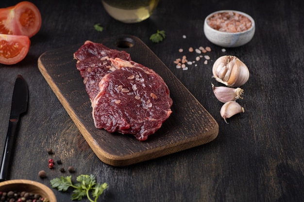 Condimento de filete de chuletón de carne fresca cruda y tomate fresco sobre fondo de madera