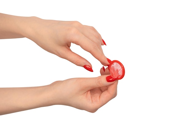 Un condón rojo en una mano de mujer con uñas rojas aislado sobre fondo blanco.