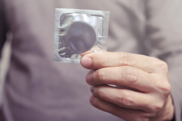 Los condones listos para usar en la mano femenina, brindan un concepto de sexo seguro del condón en la cama, evitan infecciones y los anticonceptivos controlan la tasa de natalidad o son profilácticos seguros. Día Mundial del SIDA, deje espacio para el texto.