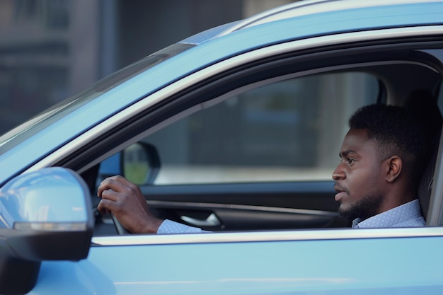 El conductor afroamericano serio se sienta en la cabina del auto