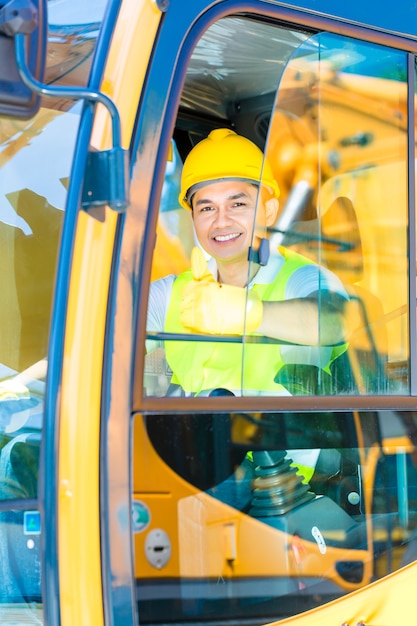 Conductor asiático sentado en la cabina de la maquinaria de construcción del sitio de construcción