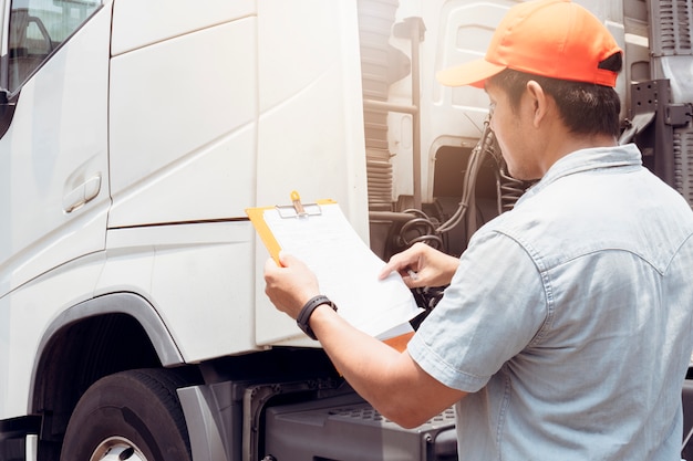 Conductor de camión asiático con portapapeles inspeccionando la lista de verificación de mantenimiento del vehículo de seguridad de camión semi
