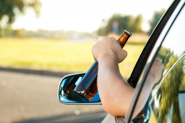 Conductor de coche sosteniendo una botella de cerveza