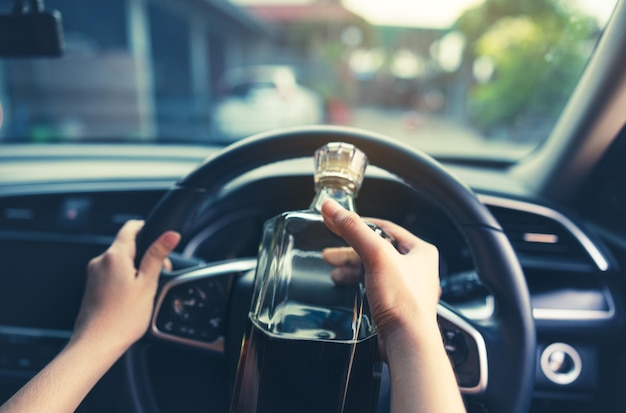 Foto el conductor está conduciendo un coche con una botella de whisky en la mano borracho concepto de conducción