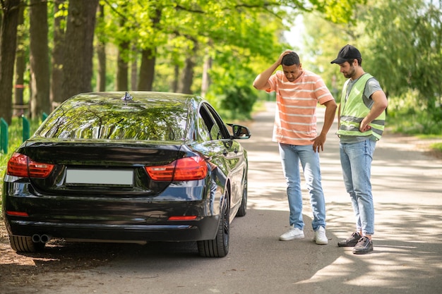 Un conductor discutiendo un accidente automovilístico con un hombre de servicio y luciendo inseguro