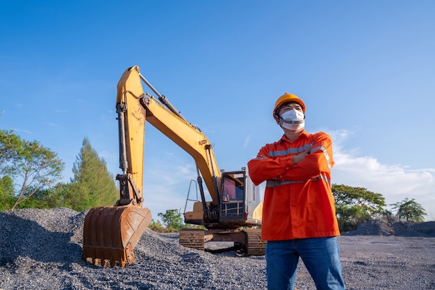 Conductor con excavadora de cadenas excavando en el sitio de construcción detrás de él sobre fondo de cielo azul