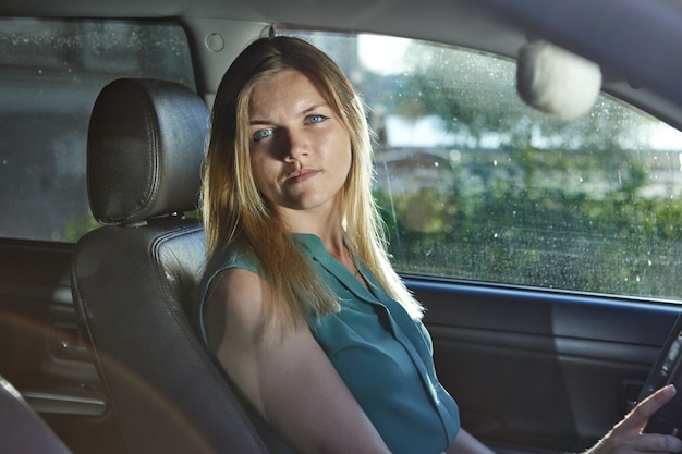 Conductor femenino con cabello rubio está sentado en el asiento del automóvil durante la conducción.