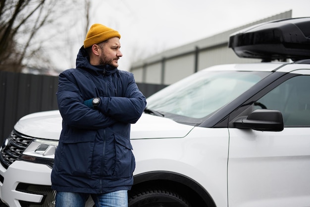 El conductor del hombre usa chaqueta y sombrero amarillo contra su automóvil SUV americano con portaequipajes en clima frío