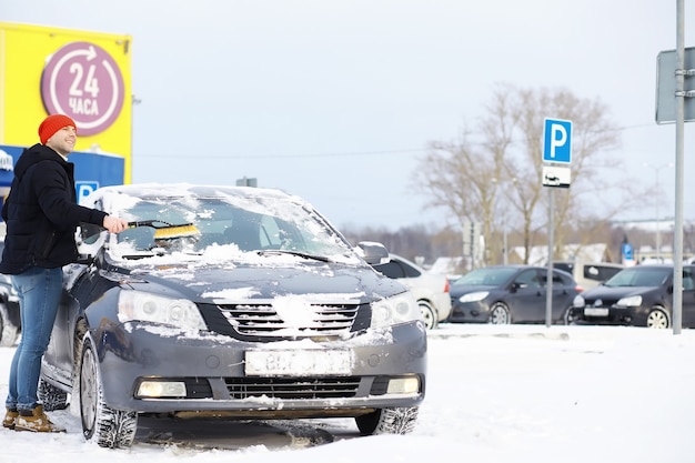 Un conductor masculino está parado frente a un automóvil. El propietario limpia el coche de la nieve en invierno. Coche después de una nevada.