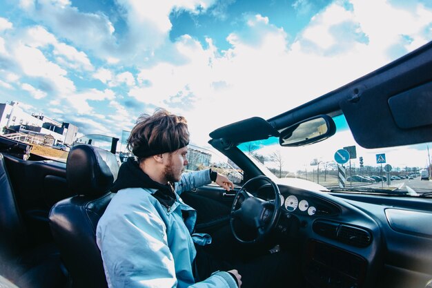 Conductor masculino viaja en un convertible por la ciudad.