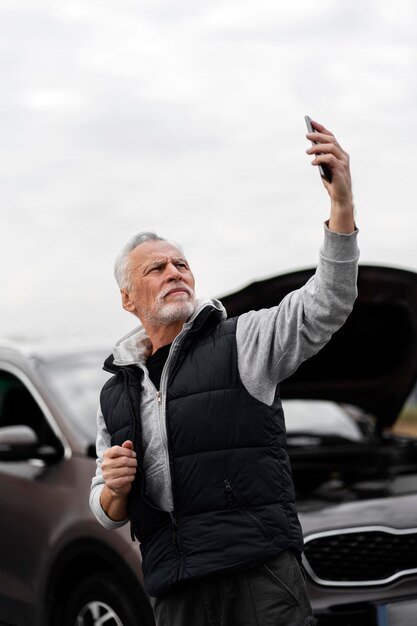 El conductor mayor usa el teléfono para explicar el problema a la asistencia en carretera a través de un enlace de video mientras se descompone