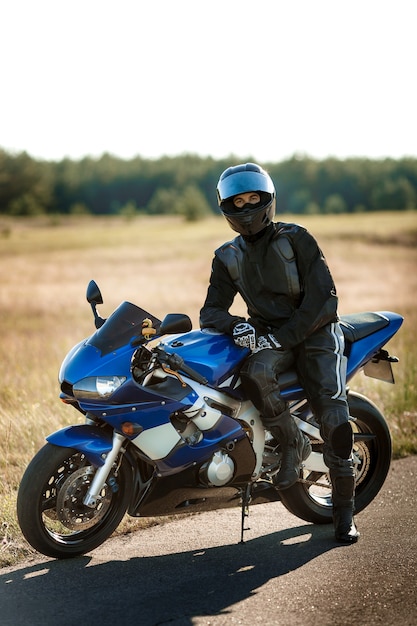 Conductor de motocicleta en casco y chaqueta de cuero se sienta en motocicleta deportiva en la carretera contra el fondo del bosque. Hermoso fondo, un lugar para copiar espacio.