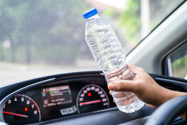 Conductor de mujer asiática sosteniendo una botella para beber agua mientras conduce un coche