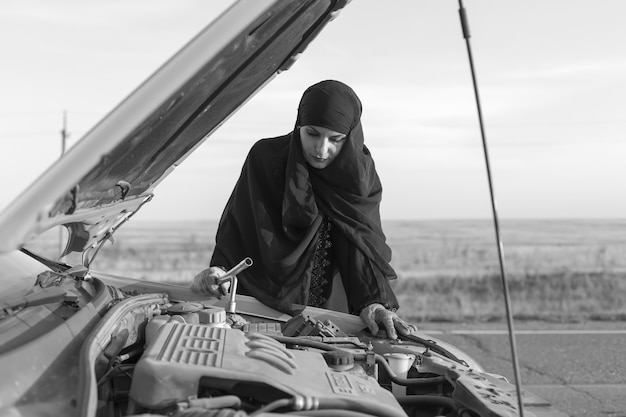 Conductor de mujer islámica que repara el coche en la carretera vacía. En blanco y negro