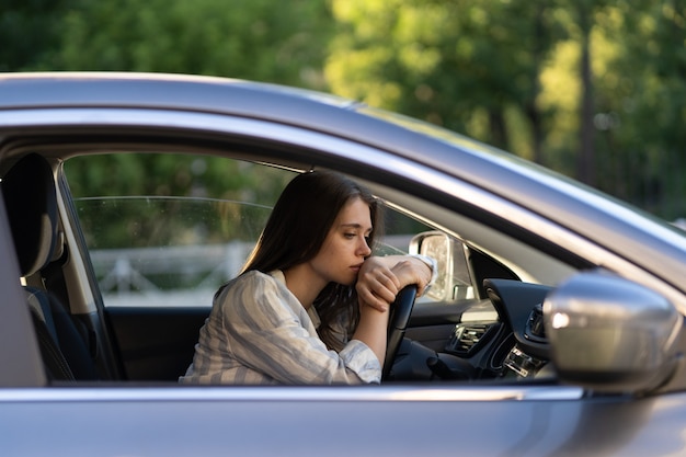 Conductor de mujer joven deprimida sentada dentro del automóvil, sintiéndose dudoso confundido acerca de una decisión difícil que sufre de un problema psicológico personal, agotamiento, pelea, ruptura con su novio, crisis de vida