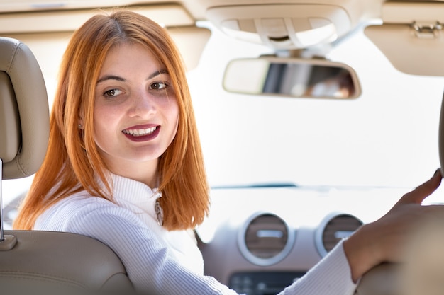 Conductor de mujer joven pelirroja conduciendo un coche sonriendo felizmente.