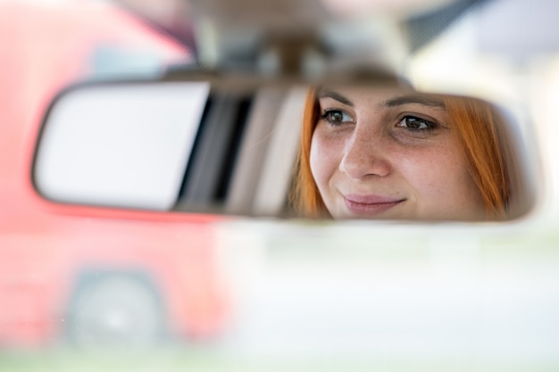 Conductor de la mujer joven que controla el espejo retrovisor que mira hacia atrás mientras conduce un coche.