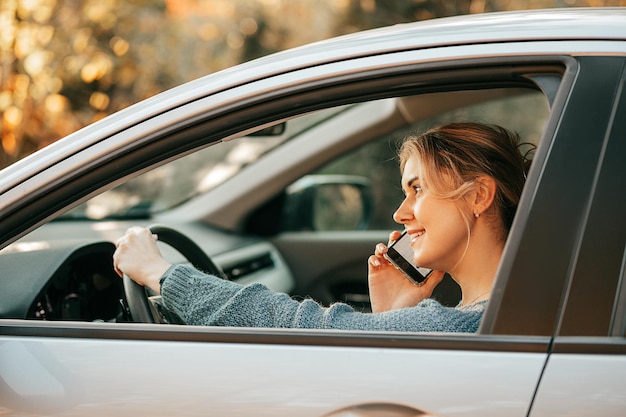 Conductor mujer rubia está hablando por teléfono inteligente detrás del volante del coche sin conducir con atención