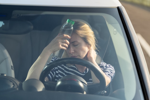 Conductor de niña agotada que sufre de dolor de cabeza calor calor aplica una botella de agua a la frente