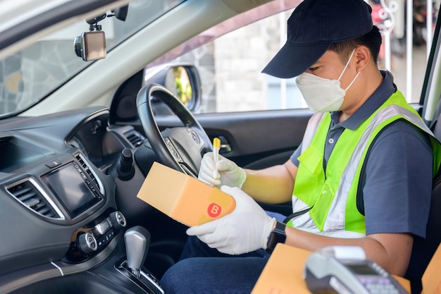 El conductor de reparto masculino asiático con una caja de cartón en el asiento del automóvil y la caja del paquete está impulsando la entrega de los clientes que compran en línea bajo la pandemia de coronavirus COVID-19