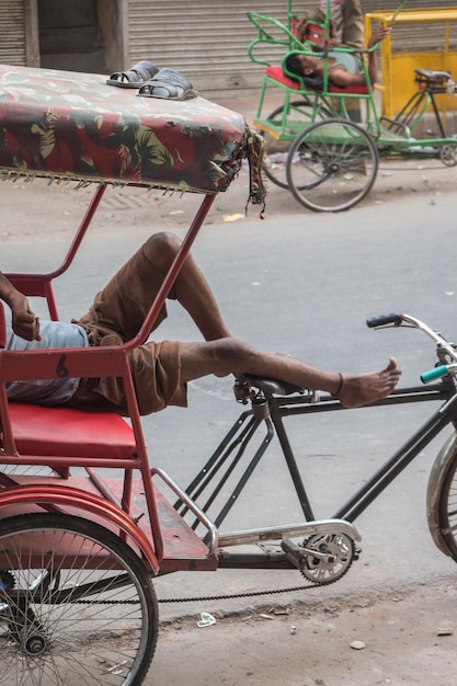 Foto el conductor de richshaw duerme en su bicicleta y mantiene los zapatos sobre el techo en la vieja delhi, india.