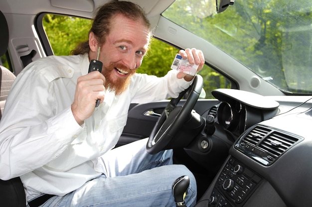 Conductor sonriendo sentado en el auto y mostrando nuevas llaves y licencia de conducir