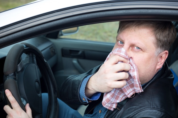 El conductor se tapó la nariz con un pañuelo de los gases fuertes de la contaminación del aire del automóvil.