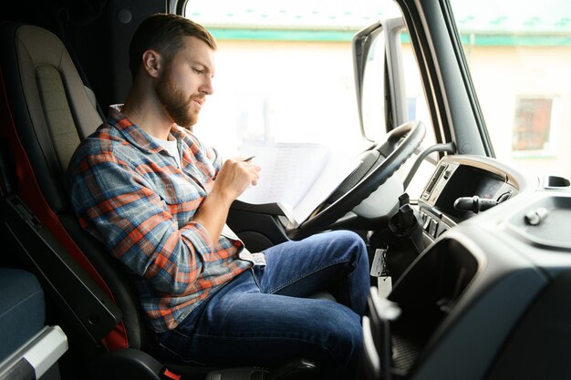 El conductor del transportista se sienta al volante de un automóvil y examina la documentación de las cartas de porte de la carga.