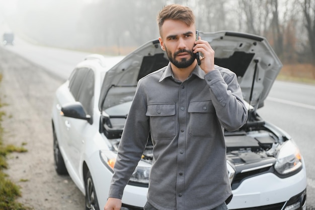 Conductor triste llamando al servicio de automóviles abriendo el capó con problemas de motor parado cerca de un automóvil roto en la carretera Concepto de avería del automóvil