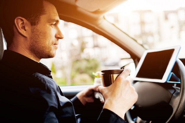 El conductor ve películas o programas de televisión en la tableta durante el almuerzo. Parando para comer algo. El hombre come merienda en el coche y bebe café o té.