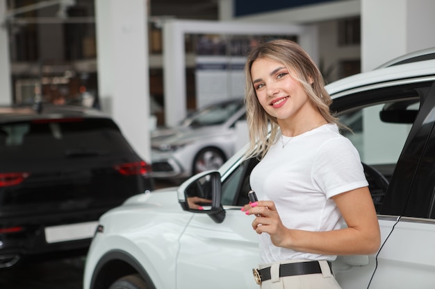 Conductora alegre posando cerca de su nuevo auto, sosteniendo la llave del auto