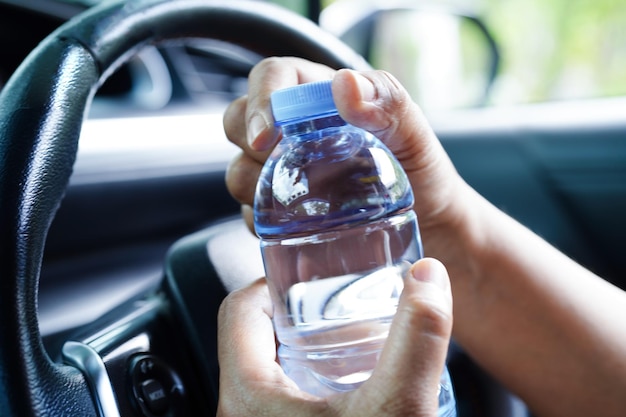 La conductora asiática sostiene agua fría para beber en un auto peligroso y corre el riesgo de sufrir un accidente