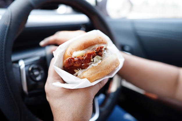 La conductora asiática sostiene y come hamburguesas en un auto peligroso y corre el riesgo de sufrir un accidente