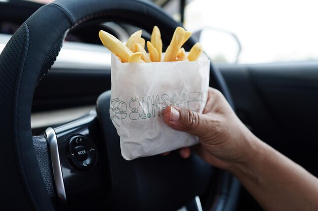 La conductora asiática sostiene y come papas fritas en un auto peligroso y corre el riesgo de sufrir un accidente